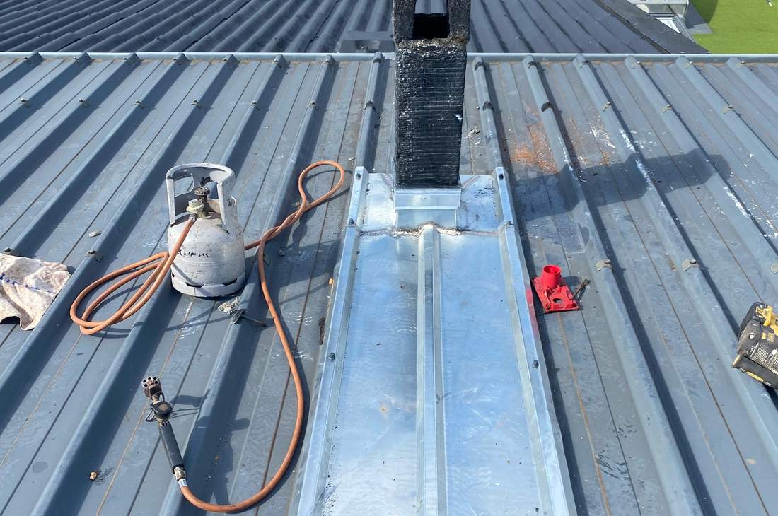 Couverture en bac acier : abergement en zinc au pied d'un conduit, bouteille de gaz et chalumeau posés sur la tôle