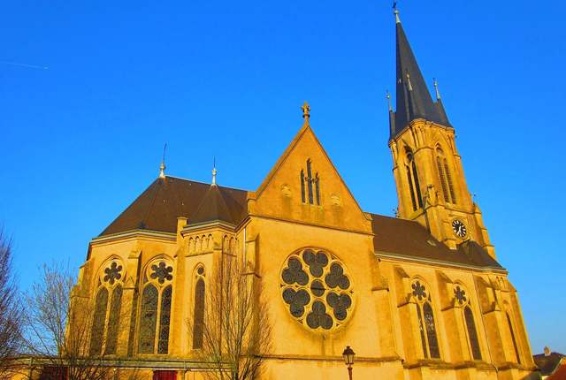 Église de Basse-Ham, pierre ocre et flèche d'ardoise, éclairée par le soleil couchant