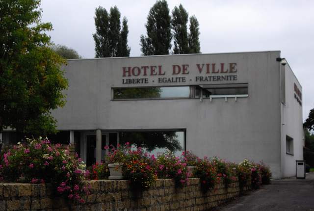 Hôtel de ville de Bousse, bâtiment moderne blanc derrière un muret fleuri