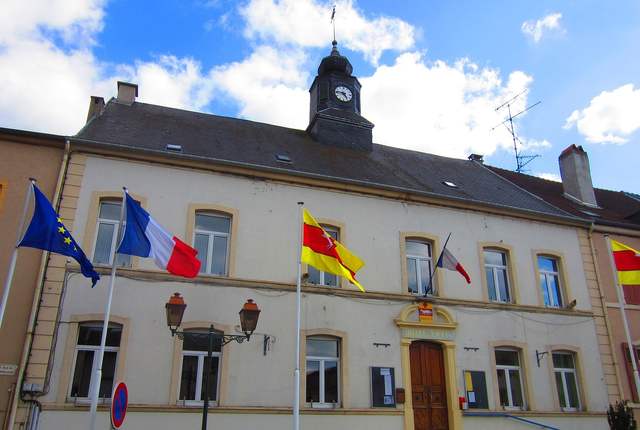 Mairie de Bouzonville, façade claire à drapeaux et lampadaires