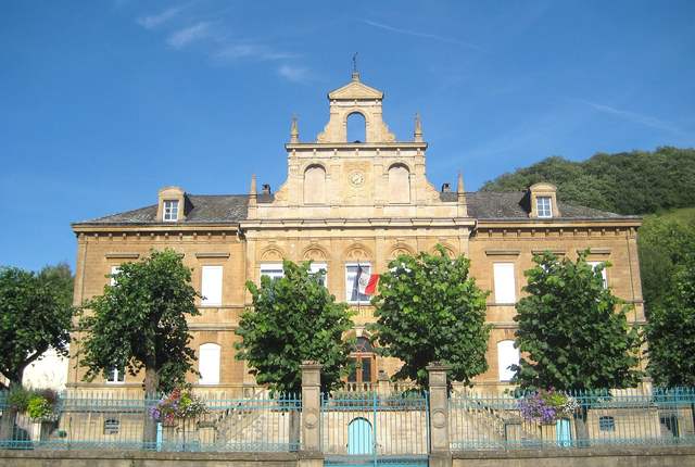 Mairie de Fontoy, façade en pierre jaune à fronton derrière des arbres taillés