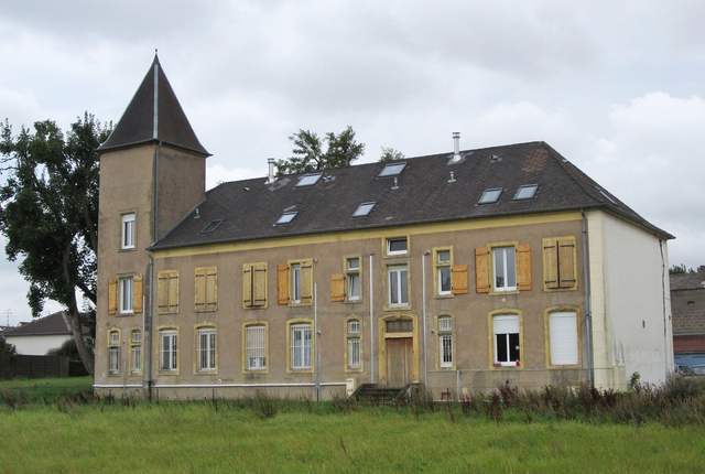 Château de Guénange, longue façade ocre à tourelle d'angle dans un pré