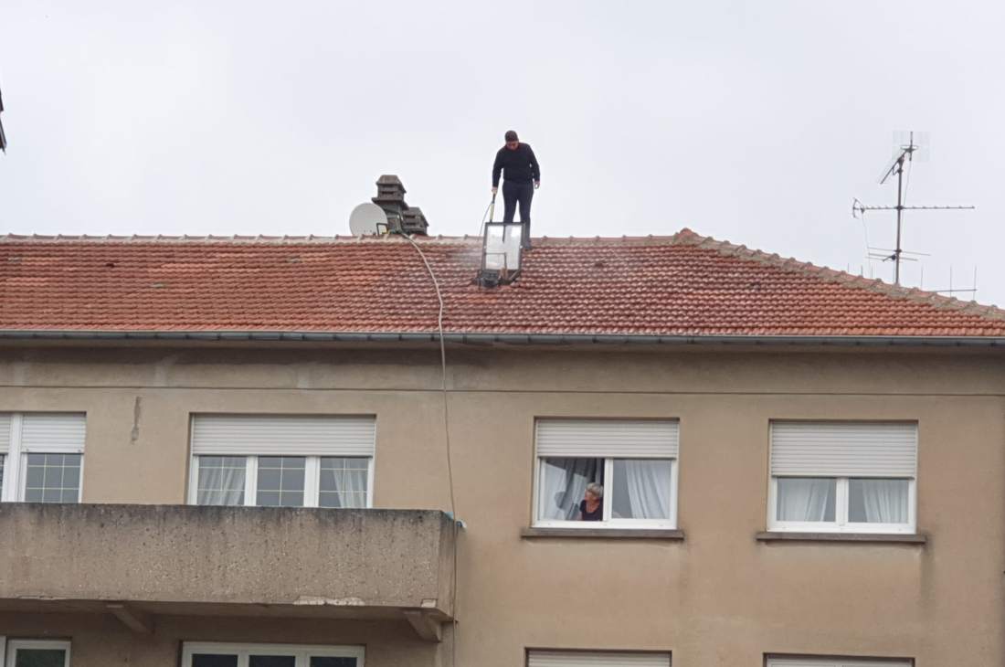 Couvreur debout sur le faîtage d'un immeuble, antenne et toits voisins autour