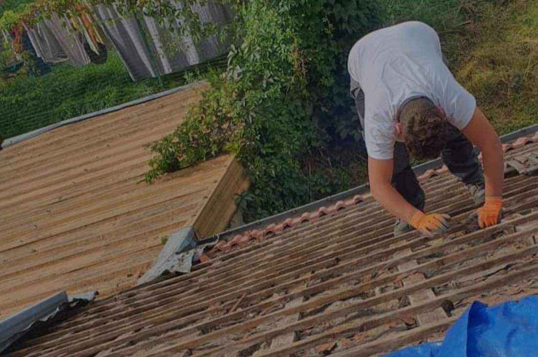 Couvreur en train de déposer des tuiles sur un toit protégé par une bâche
