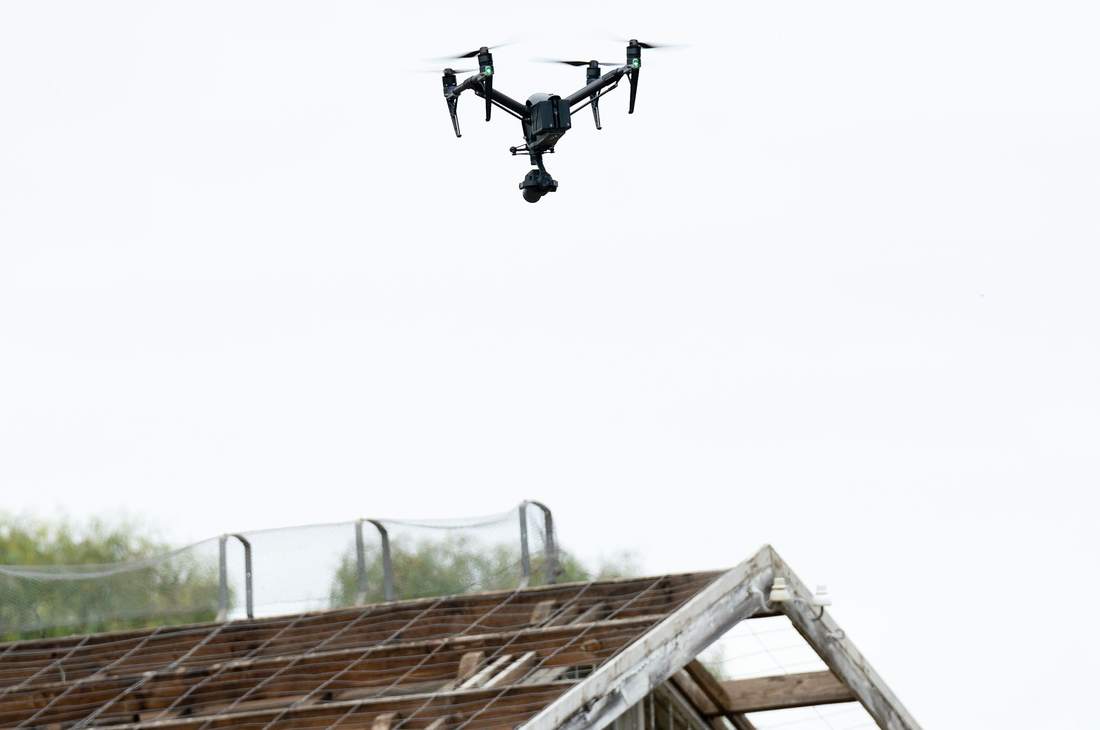 Drone en vol stationnaire au-dessus d'une toiture déposée, liteaux apparents