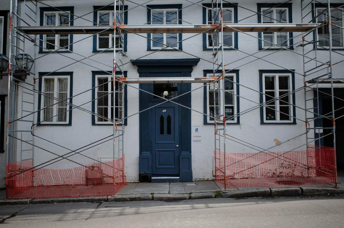 Façade blanche sous échafaudage, filet de protection orange au pied