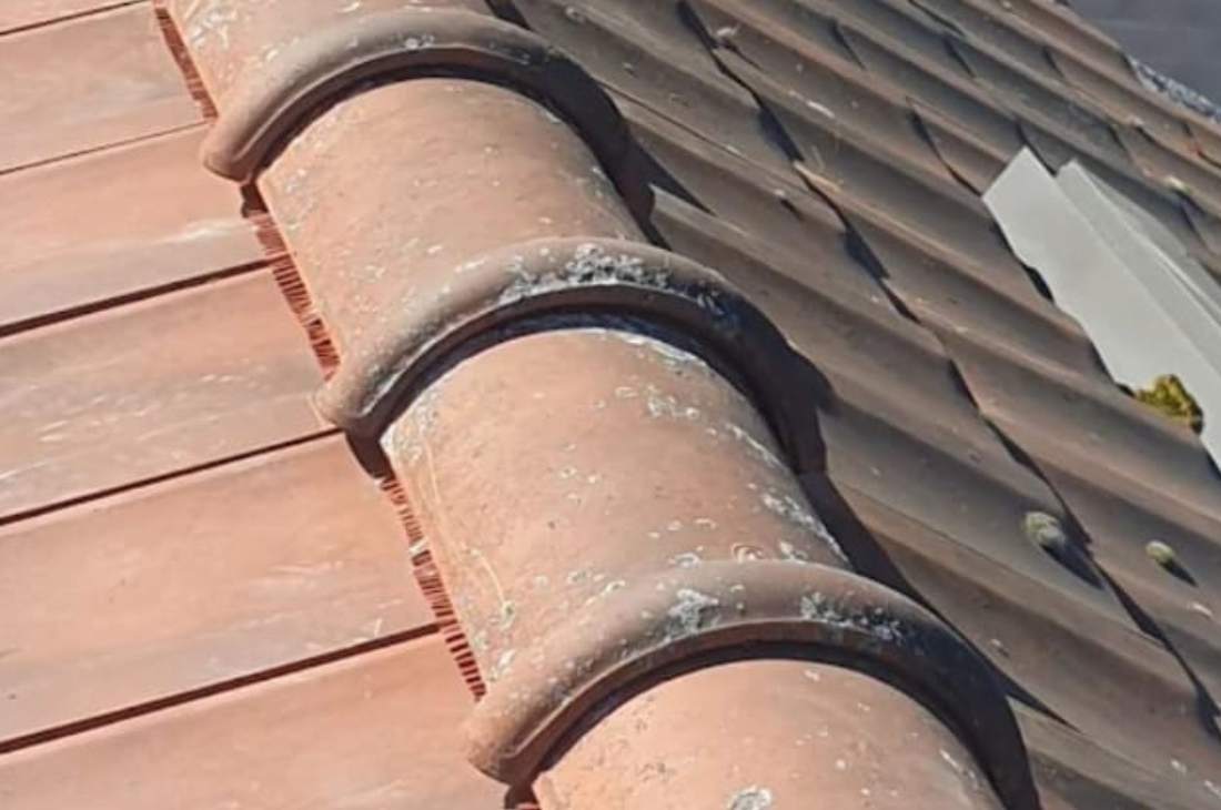 Rang de tuiles faîtières scellées au mortier, à la jonction entre une couverture en tuiles et des plaques ondulées