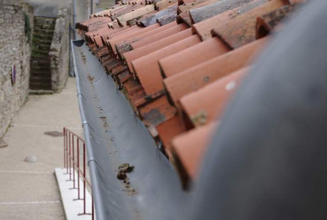 Gouttière demi-ronde en zinc le long d'un toit en tuiles, maison de bourg en pierre