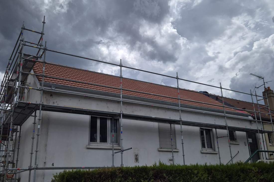 Maison sous échafaudage pendant la réfection de sa toiture en tuiles, sous un ciel chargé