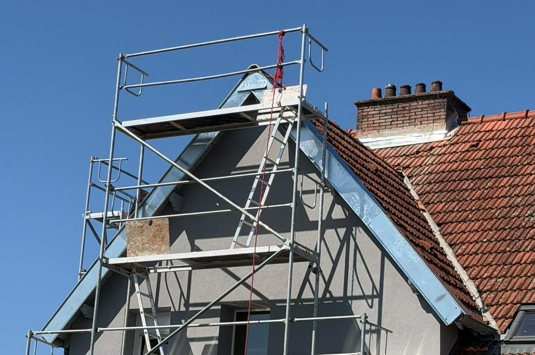 Maison sous échafaudage, pignon enduit bordé d'une rive en zinc, toiture en tuiles sous un ciel bleu
