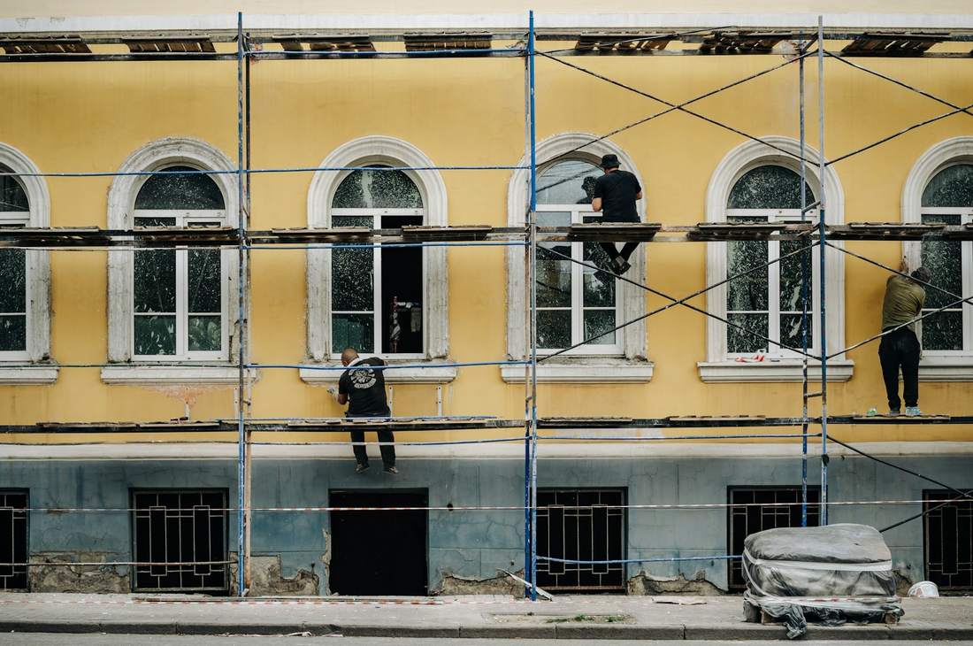 Ouvriers sur l'échafaudage d'une façade jaune à fenêtres cintrées