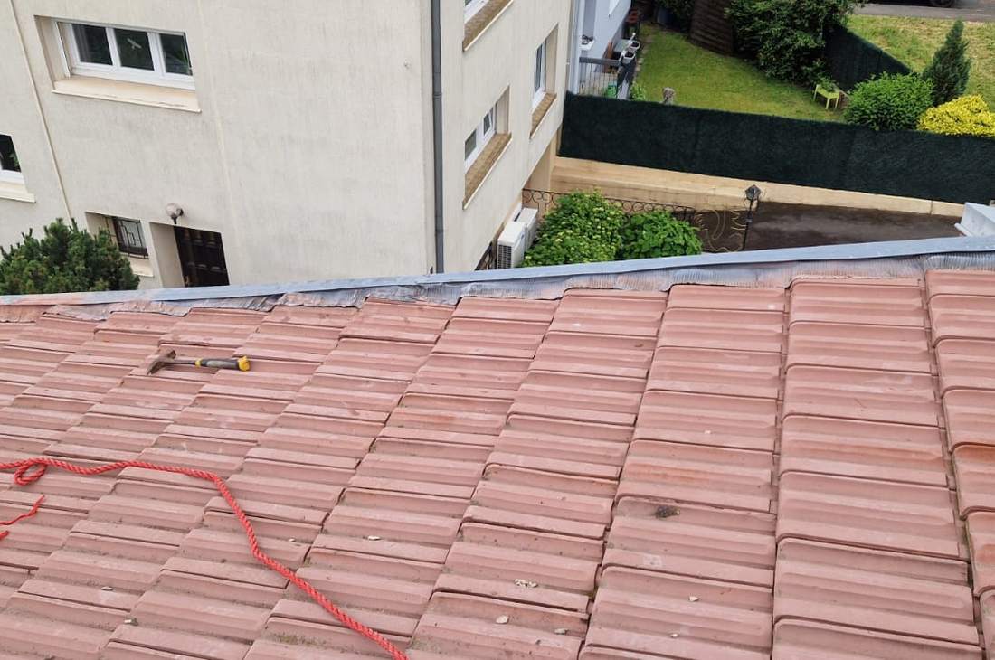 Pan de toiture en tuiles rouges avec cordage de sécurité tendu le long de la rive
