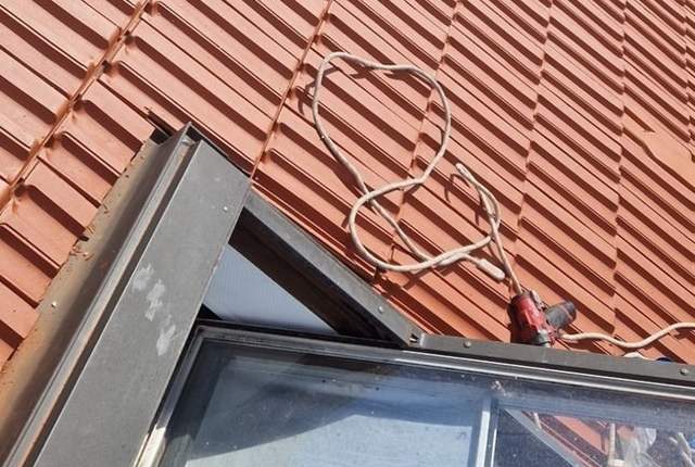Pan de tuiles rouges vu depuis une fenêtre de toit ouverte, corde de sécurité posée sur les tuiles