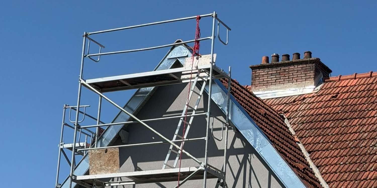 Pignon de maison sous échafaudage, rive en zinc et toiture en tuiles sous un ciel bleu