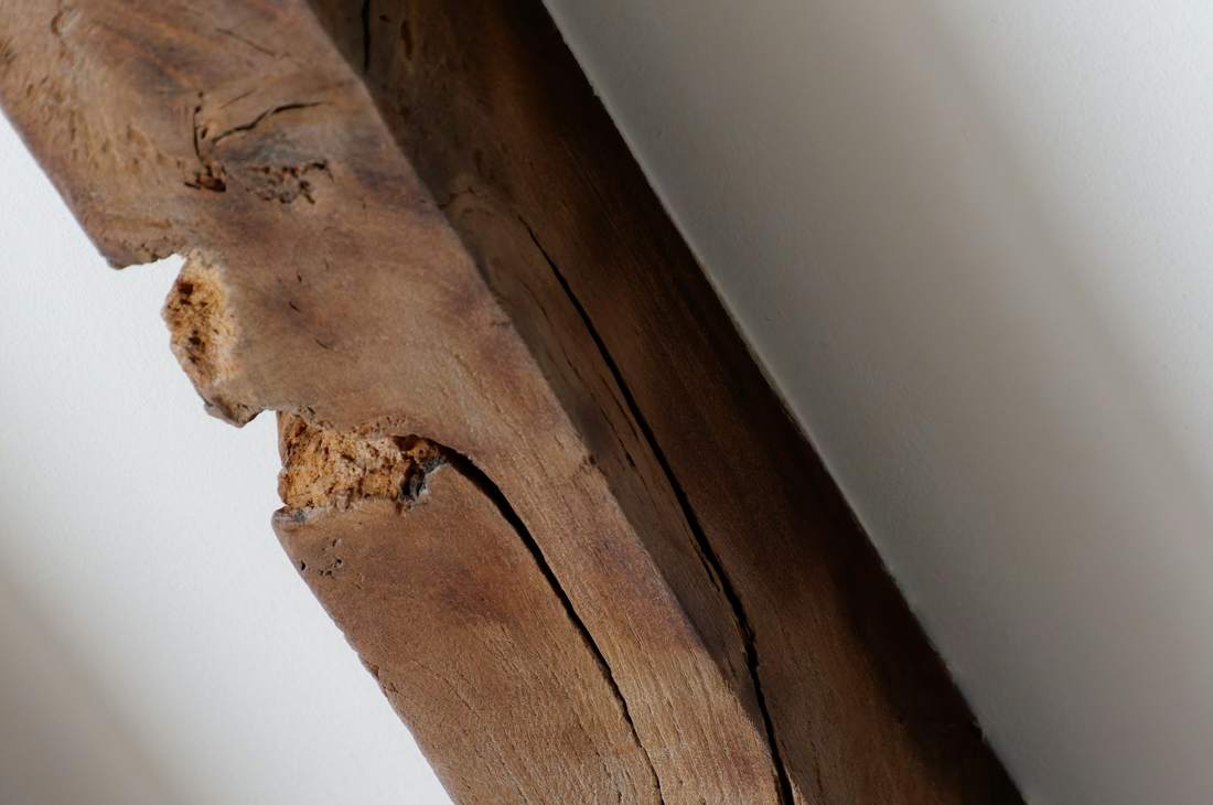 Poutre ancienne fendue et entamée sur une arête, contre un plafond blanc