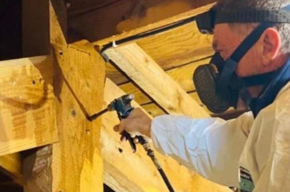 Opérateur en combinaison et masque respiratoire pulvérisant un produit de traitement sur une charpente
