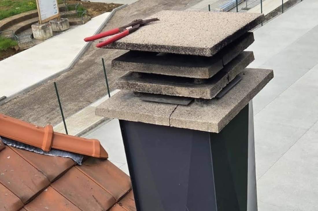 Souche de cheminée habillée de zinc anthracite sous son chapeau en béton, pince posée sur le dessus
