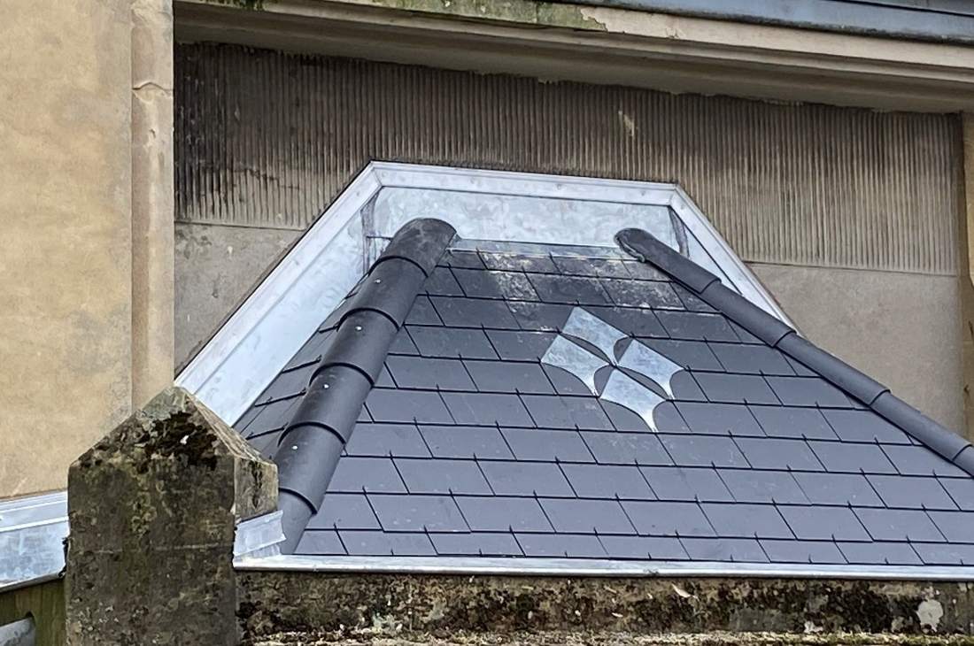 Petit toit en ardoise à motif losangé, arêtiers arrondis et habillage en zinc contre la façade
