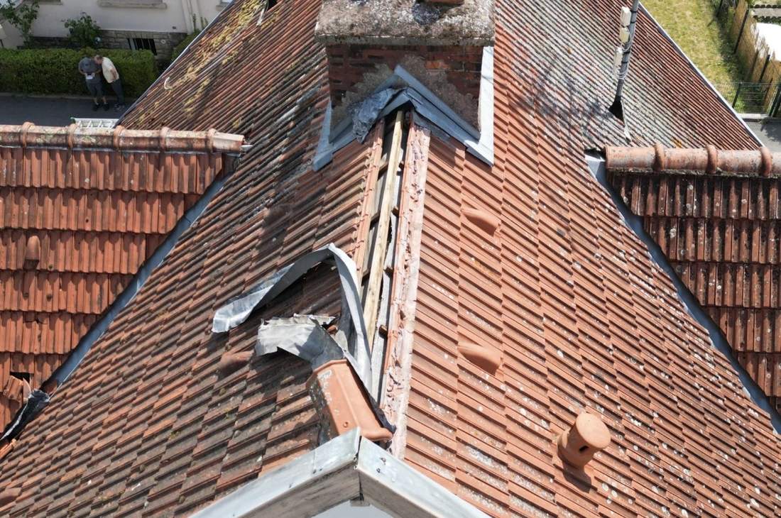 Toiture en tuiles vue d'en haut : faîtage abîmé, bandes de zinc arrachées sous la cheminée